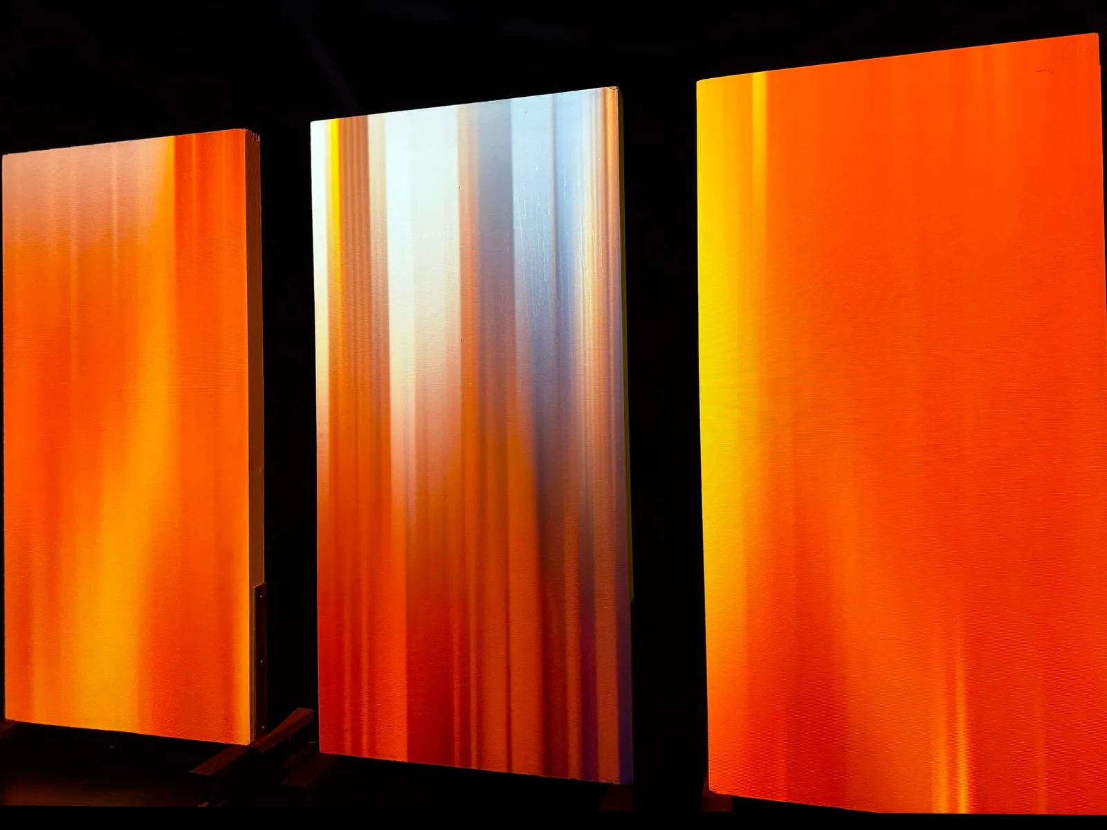 Three projection panels washed in streaking orange and white light, Nocturnal installation