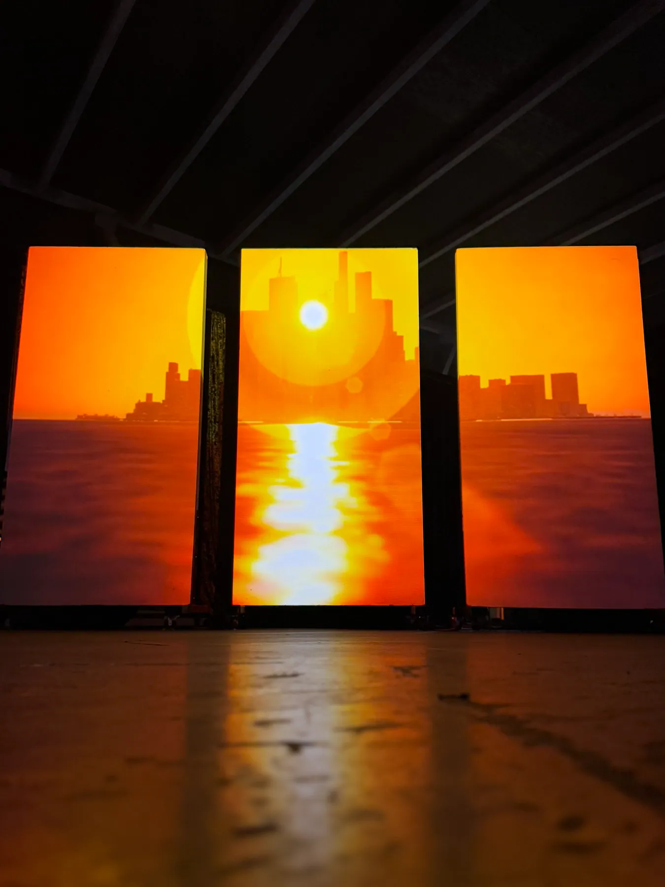 City skyline at sunset reflected on water, projected across three panels, Nocturnal installation