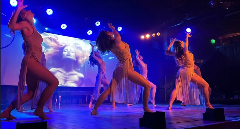 Bella Lux dancers performing in blue stage light in front of a projected visual of a woman's face