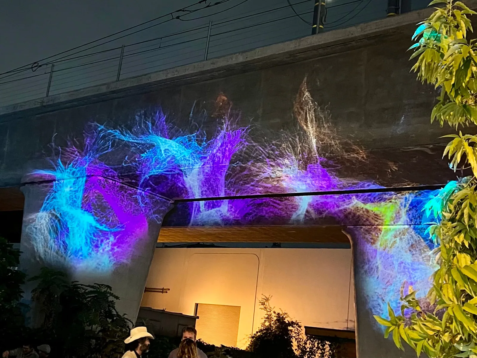 Blue and purple light-filament visuals projected on a concrete overpass wall, Culver City Arts Festival
