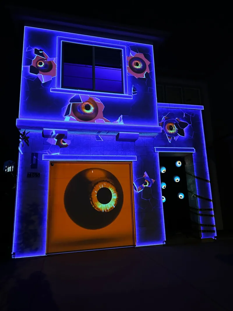 House facade outlined in blue light with projected eyes bursting through cracked walls, Halloween 2022