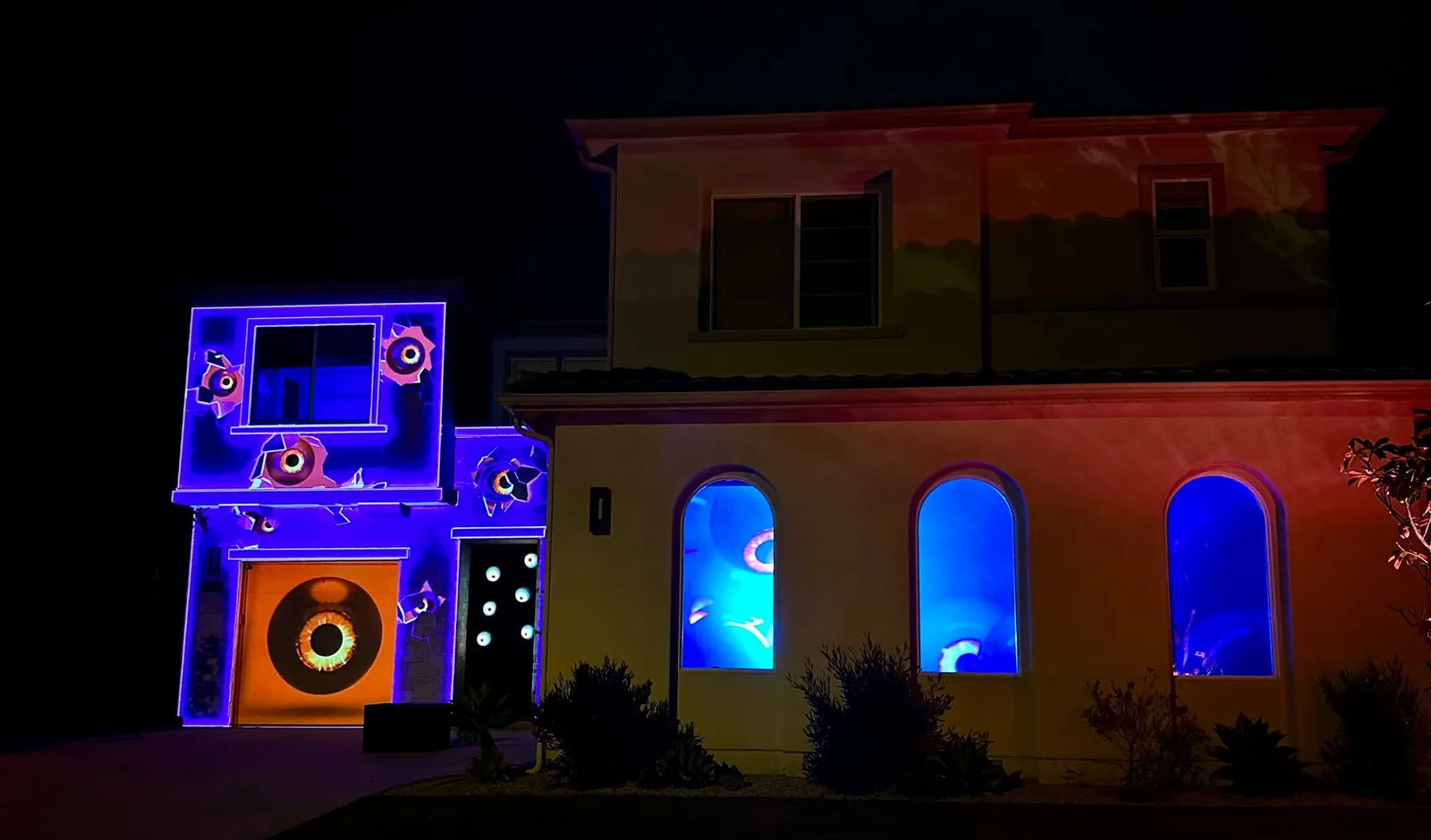 Wide view of a projection-mapped house with eyes in the walls and blue-lit arched windows, Halloween 2022