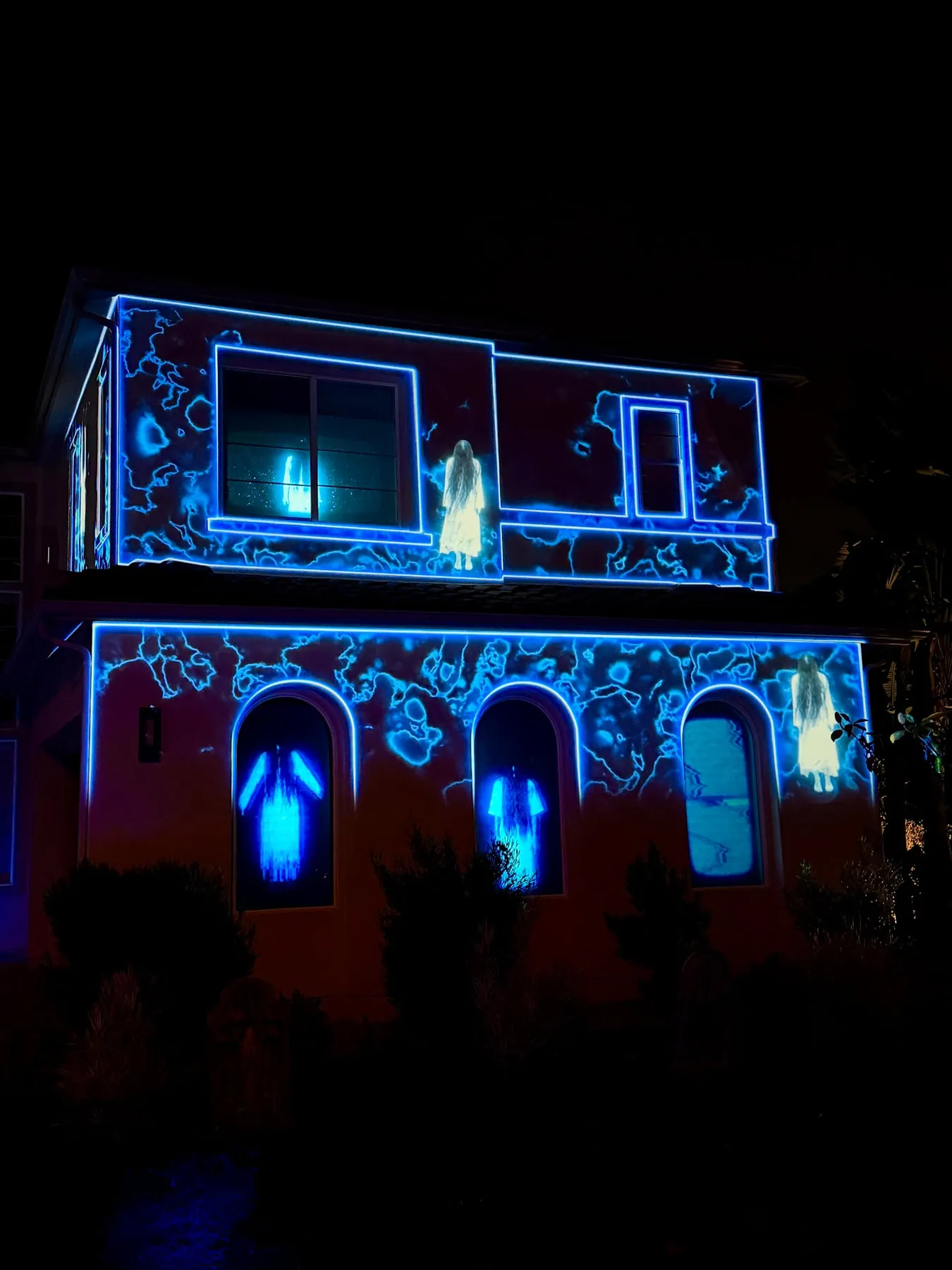 Spectral figures in the arched windows of a projection-mapped house, Halloween 2025
