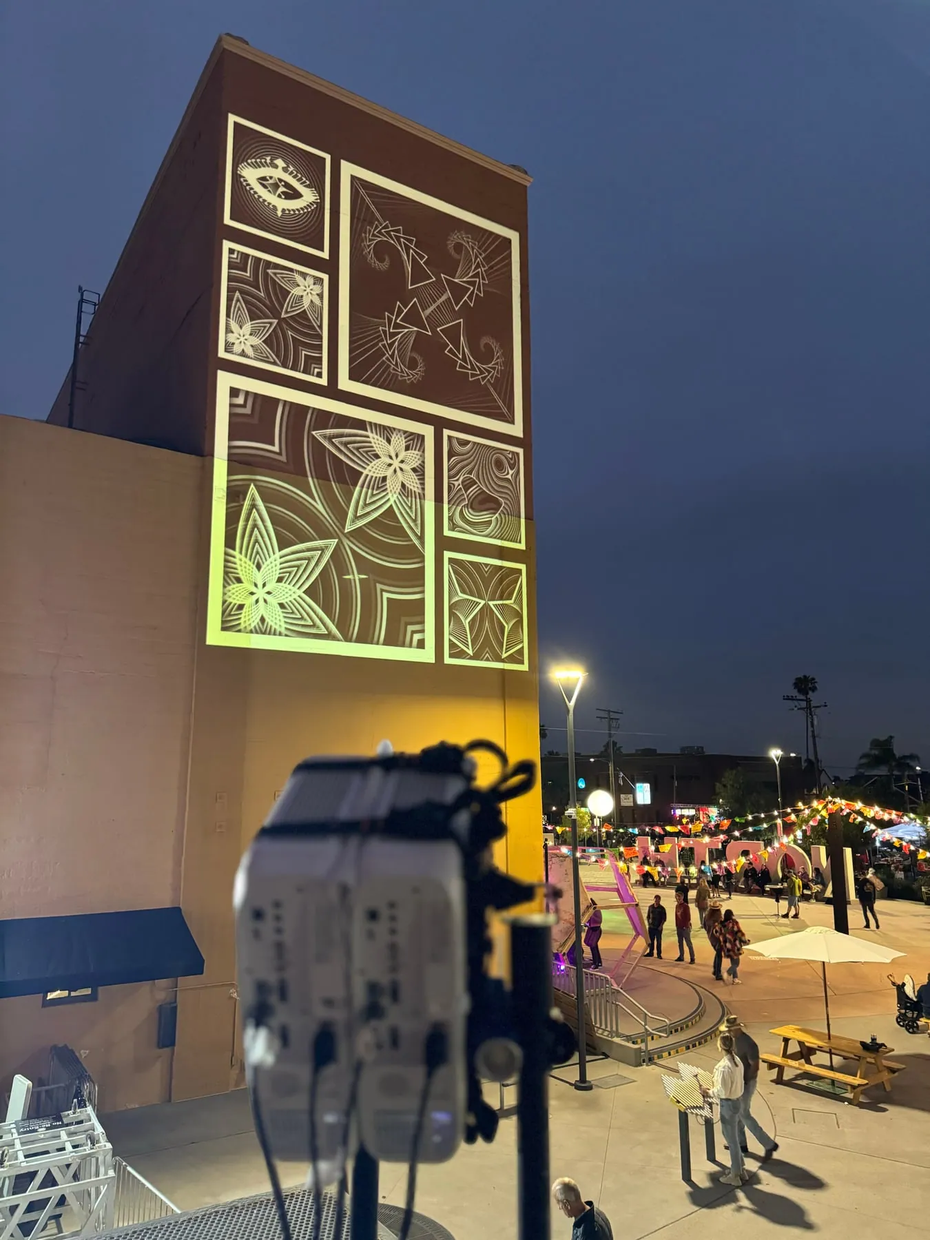 Projector in the foreground aimed at a building facade showing a projected floral mural