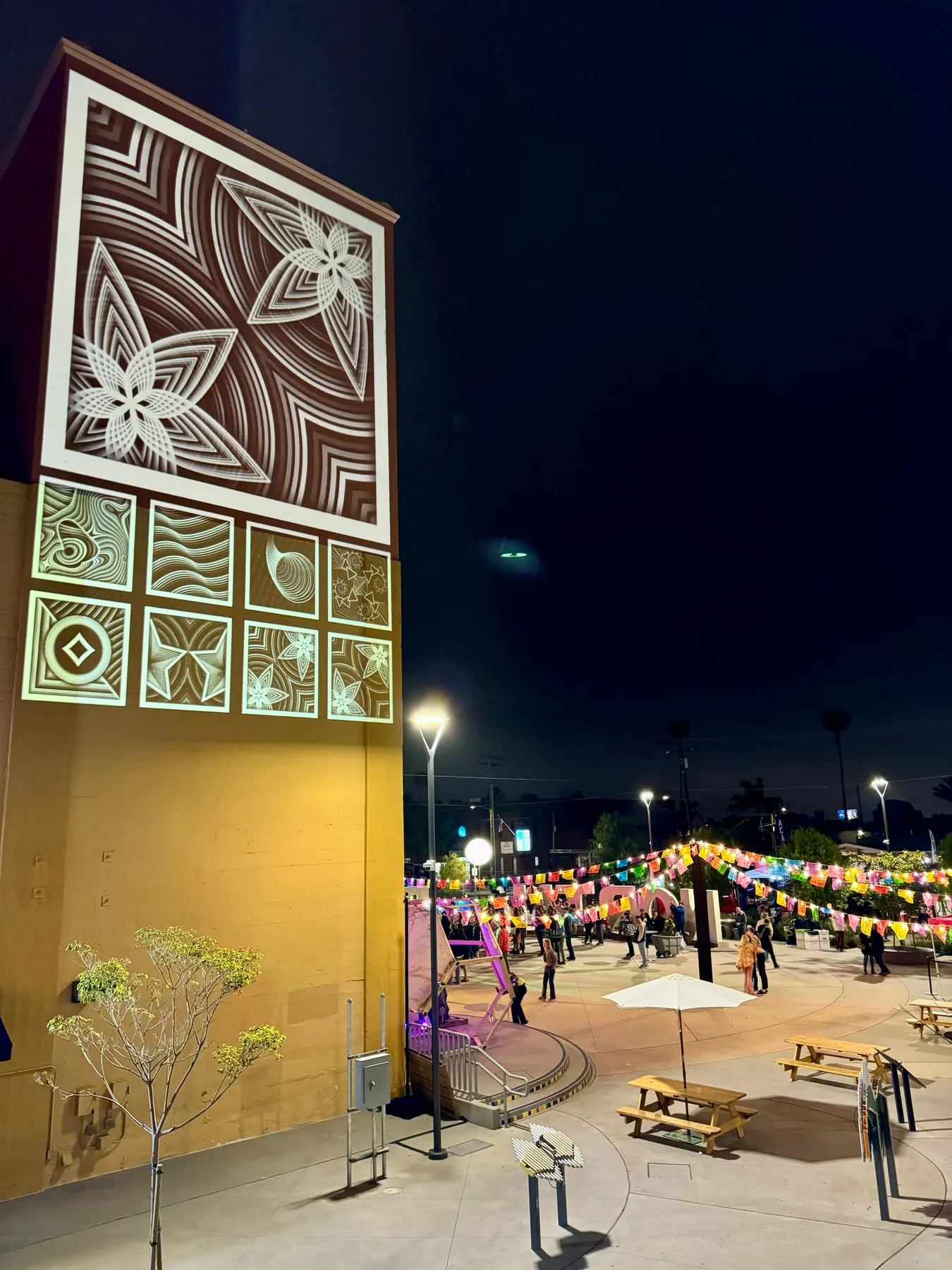 Floral line-art mural projected on a tall facade above a plaza strung with lanterns