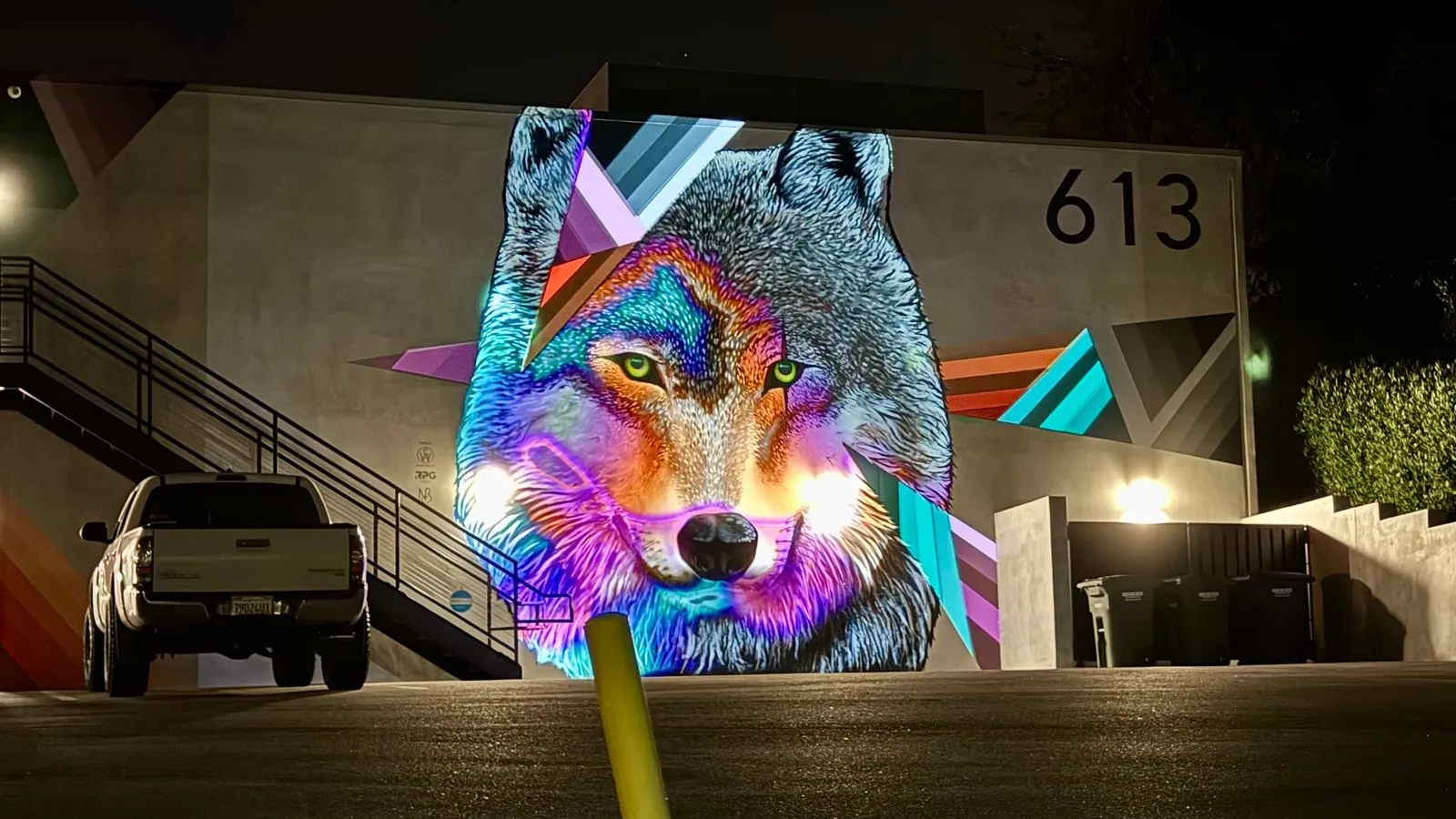 Wide night view of the projection-mapped wolf mural beside a parking lot