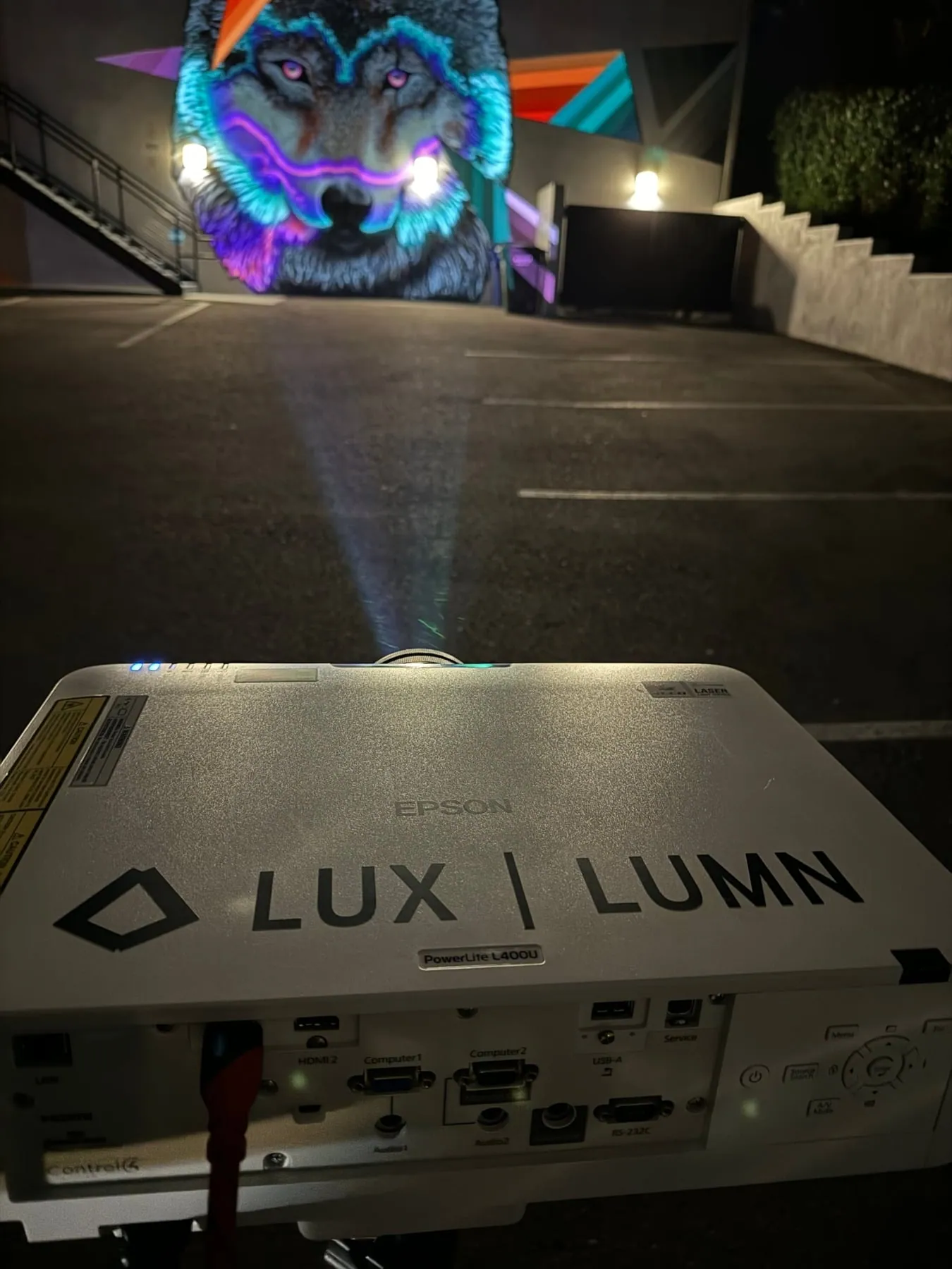 LUX LUMN projector in a parking lot aimed at the projection-mapped wolf mural